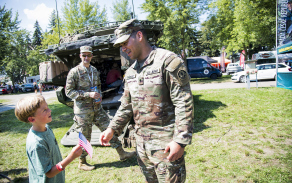 Americký voják předává vlajku USA před obrněným transportérem Stryker